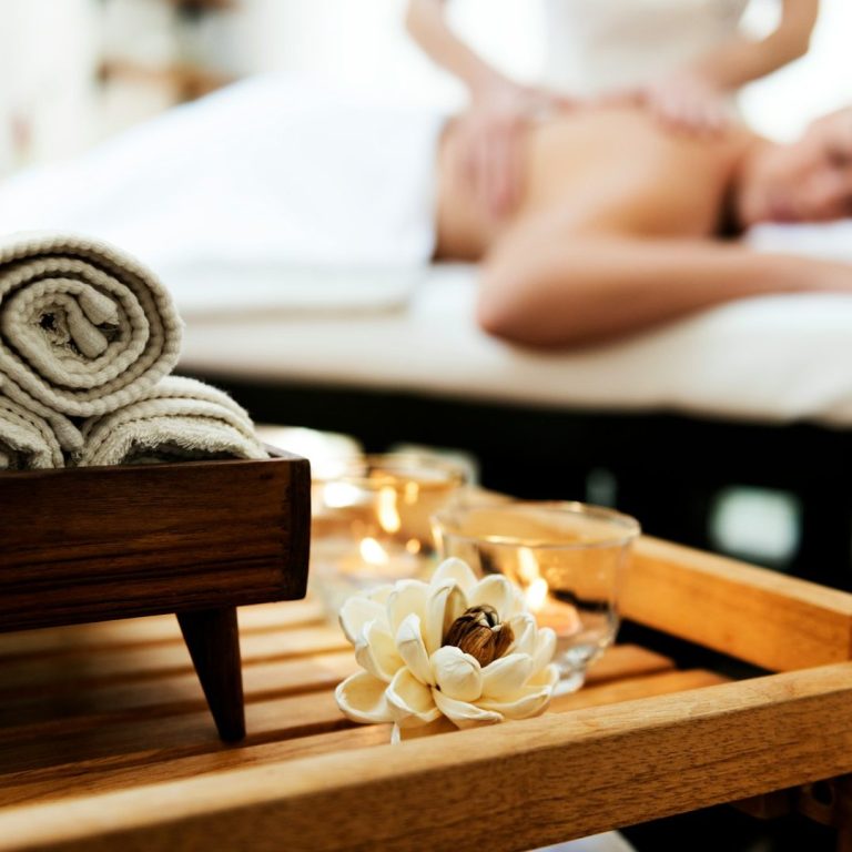 Spa setting with rolled towels, candles, and a person receiving a massage.