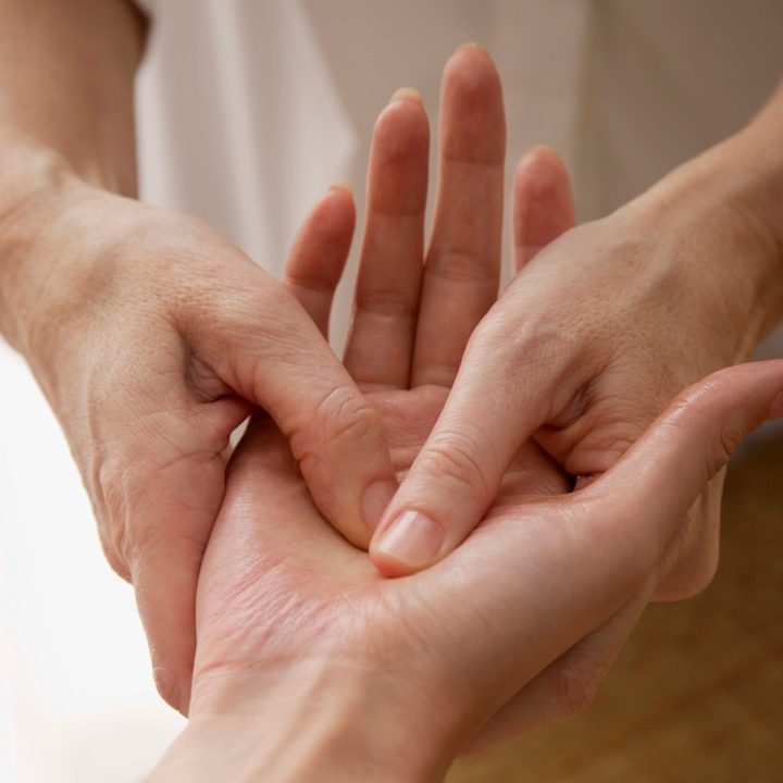 Two hands are gently massaging and examining another hand.